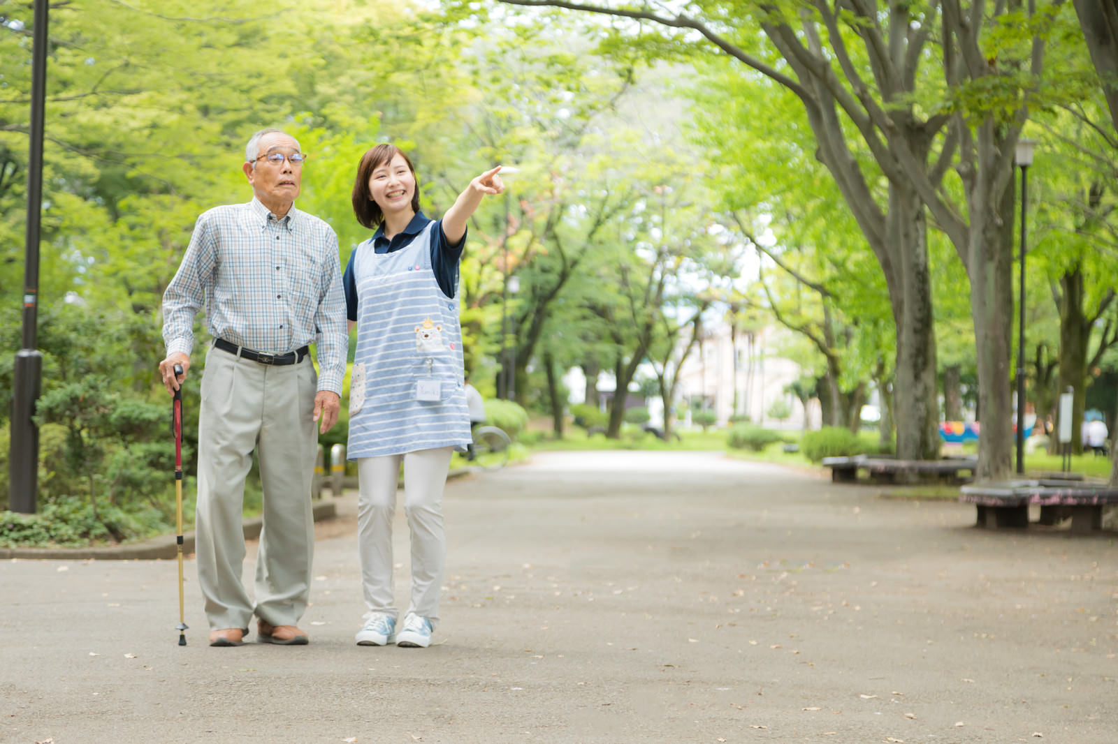 公園を散歩する高齢の男性と介護スタッフ